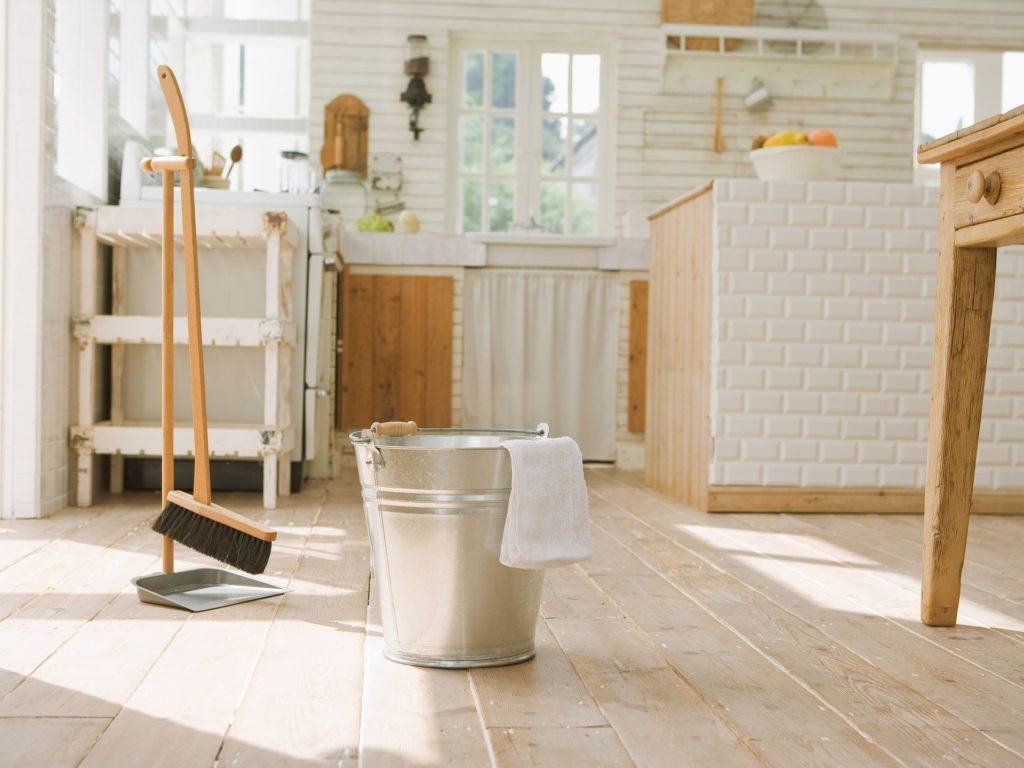 White kitchen with a broom and bucket in the foreground (Source: Canva).