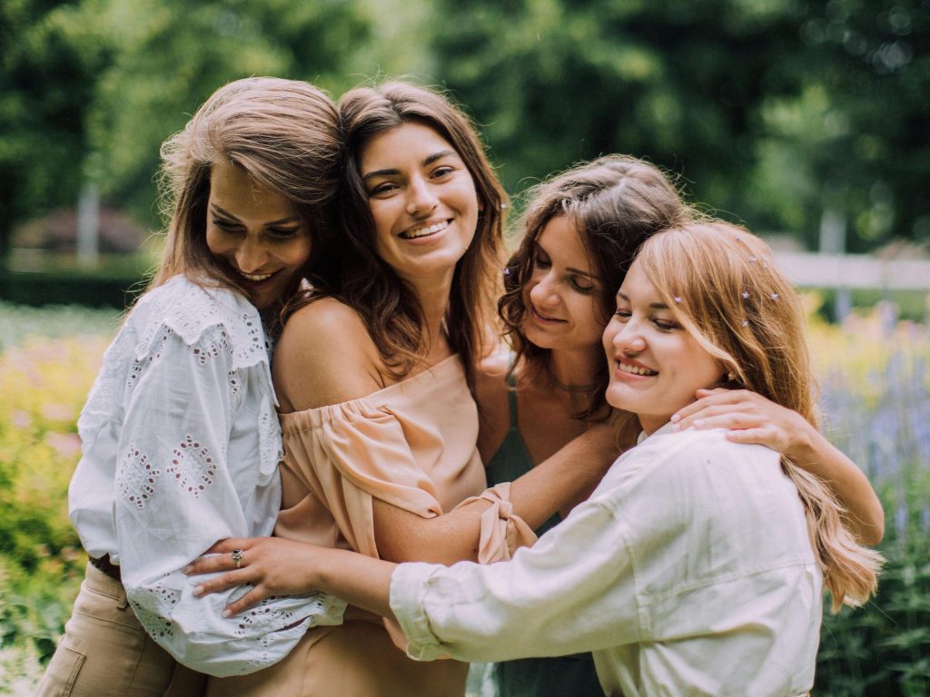 Four young women in a group hug (Source: Canva).