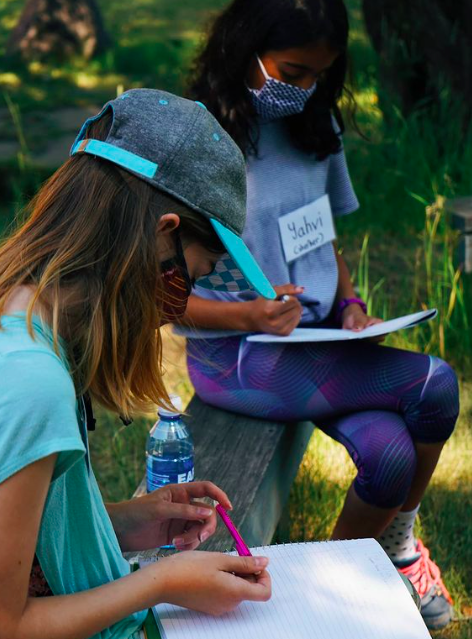 Two girls writing in notebooks outdoors.