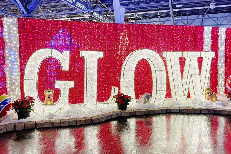 A display featuring block letters G-L-O-W in white lights in front of a wall made of red lights at the entrance of Christmas GLOW Edmonton.