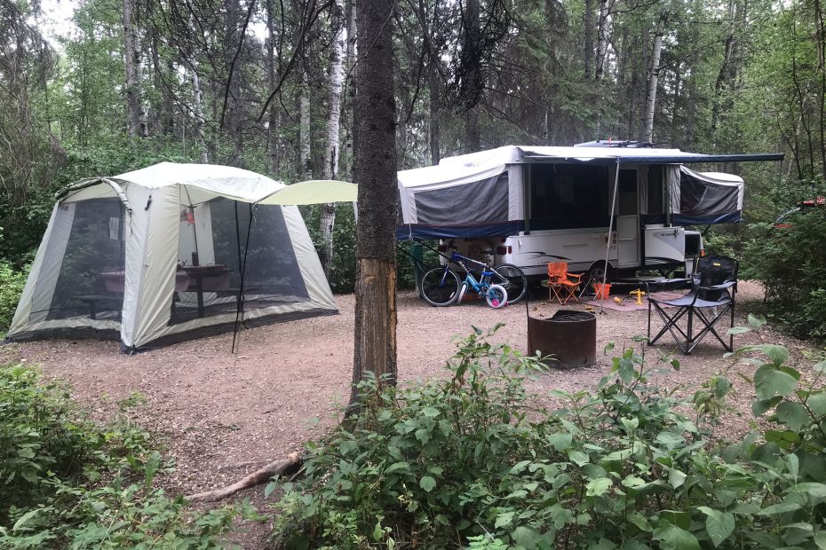 Dining tent and tent trailer set up at a campsite with bikes and camp chairs around the site.