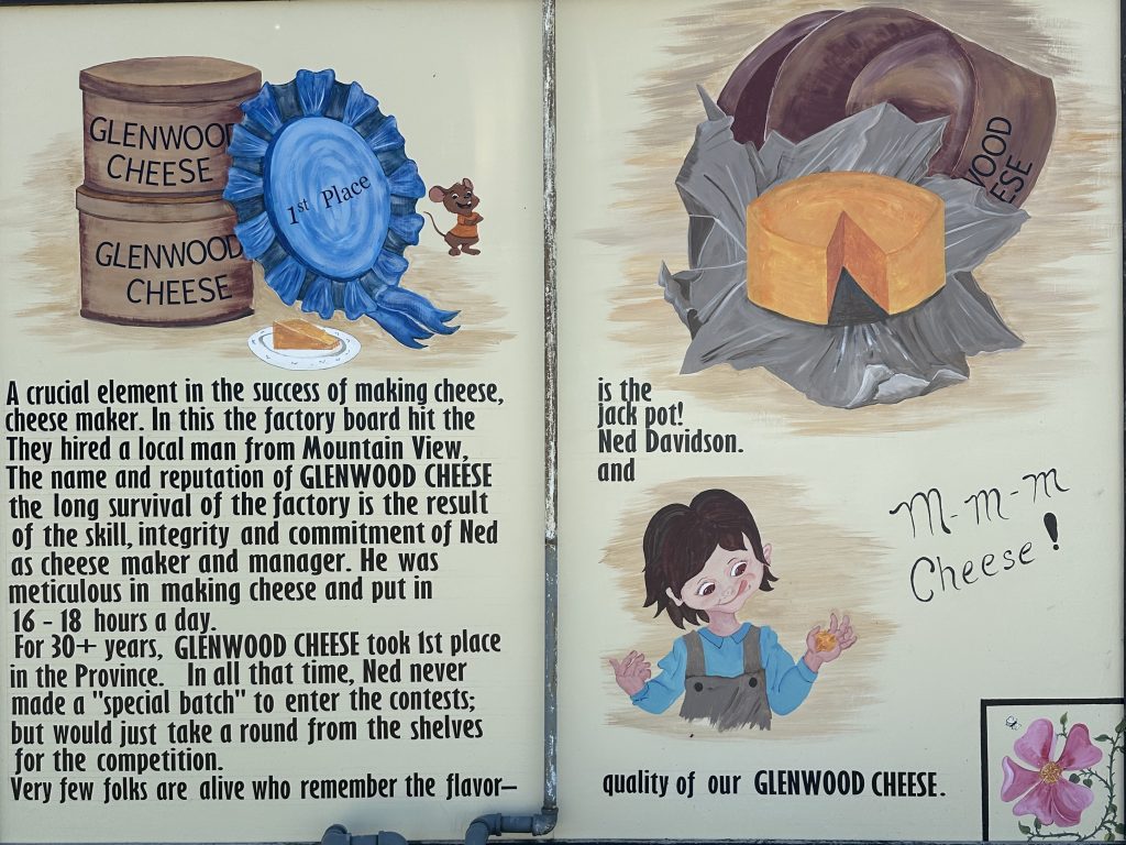 Photo of a mural outside the Cheese Factory Museum in Glenwood. Text on it reads "A crucial element in the success of making cheese, cheese maker. In this the factory board hit the They hired a local man from Mountain View The name and reputation of GLENWOOD CHEESE the long survival of the factory is the result of the skill, integrity and commitment of Ned as cheese maker and manager. He was meticulous in making cheese and put in 16 - 18 hours a day. For 30+ years, GLENWOOD CHEESE took ist place in the Province. In all that time, Ned never made a "special batch" to enter the contests; but would just take a round from the shelves for the competition. Very few folks are alive who remember the flavor- is the jack pot! Ned Davidson and quality of our GLENWOOD CHEESE."