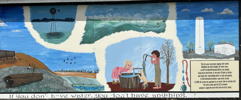 Photo of a mural outside the Fire Hall Building in Glenwood. Text reads ""If you don't have water, you don't have anything." and "The first years were hard, hauling river water.
Windmills and wells brought the water closer.
In 1919 the United Irrigation District was formed.
Using horses and fresnos, in two years 172 miles of ditches and canals were dug bringing water to crops and gardens.
In 1963 Glenwood installed a town water system.
In 1986 the system was upgraded to use water from an artesian well.
The town system and the U.I.D. network
continue to supply the area with water for all its needs."
